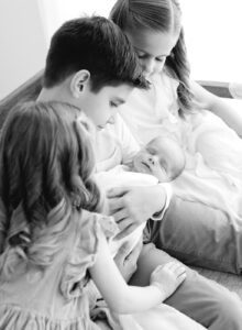black and white newborn photo with three older siblings
