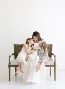 mom in long white dress on bench with her daughters