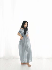 Pregnancy photo of woman in sheer dress backlit in natural light photography studio