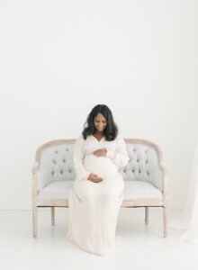 maternity photo in natural light of pregnant mom sitting on a grey sette in studio