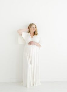 materntiy photo of woman in long white dress against a white wall