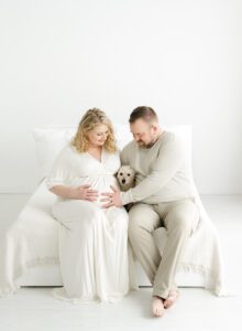Maternity photo of pregnant mom with husband and their small dog sitting on a bed