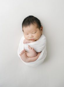 baby wrapped up in white swaddle for newborn photos