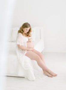 pregnant woman sitting on white bed in lacy robe