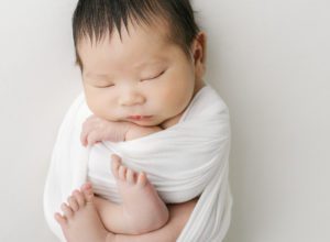 newborn baby swaddled in white wrap on white background in Minneapolis photography studio