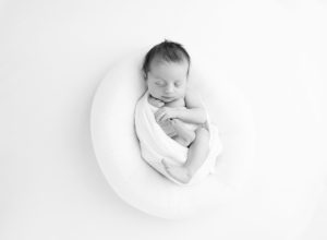 newborn baby in white swaddle sleeping on posing pillow in black and white