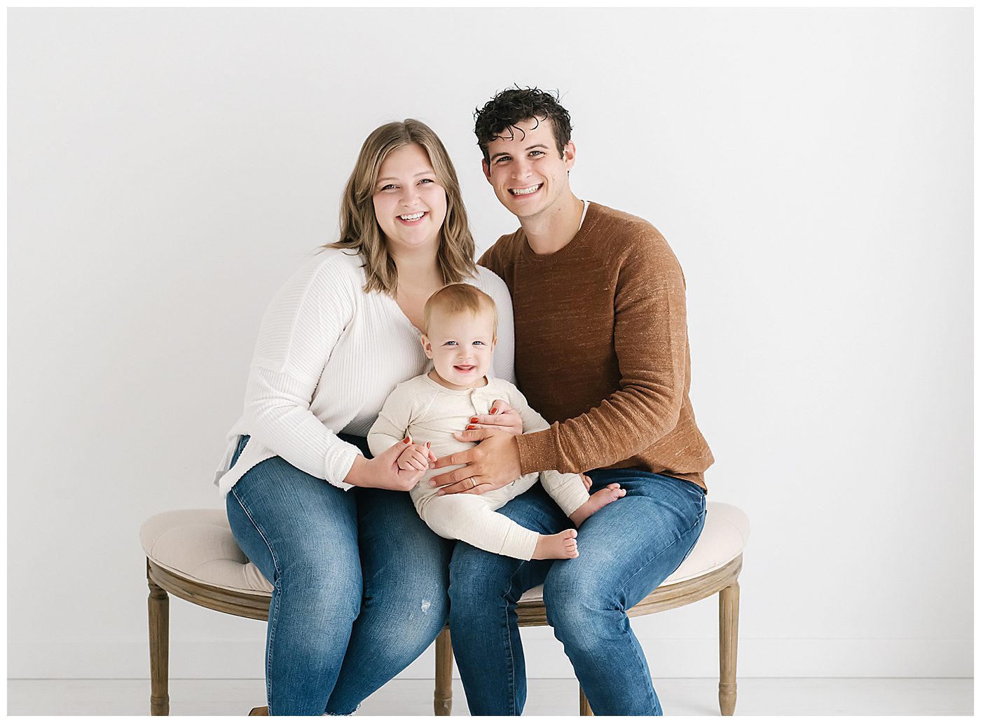 mom and dad sitting on bench with one year old baby boy in Lino Lakes photography studio