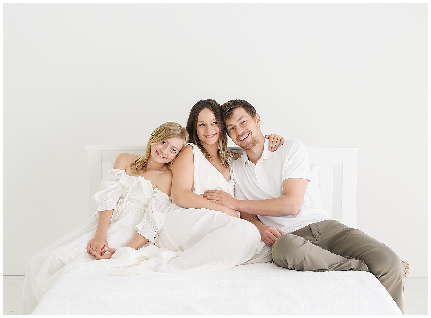 Family photo with mom, dad, pre-teen on bed in all white natural light photography studio