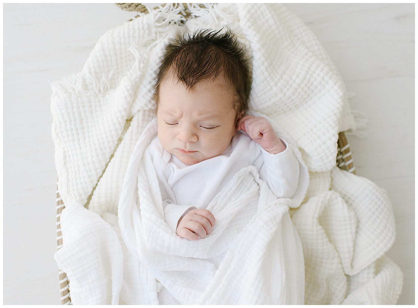 newborn baby boy in white onesie with dark hair