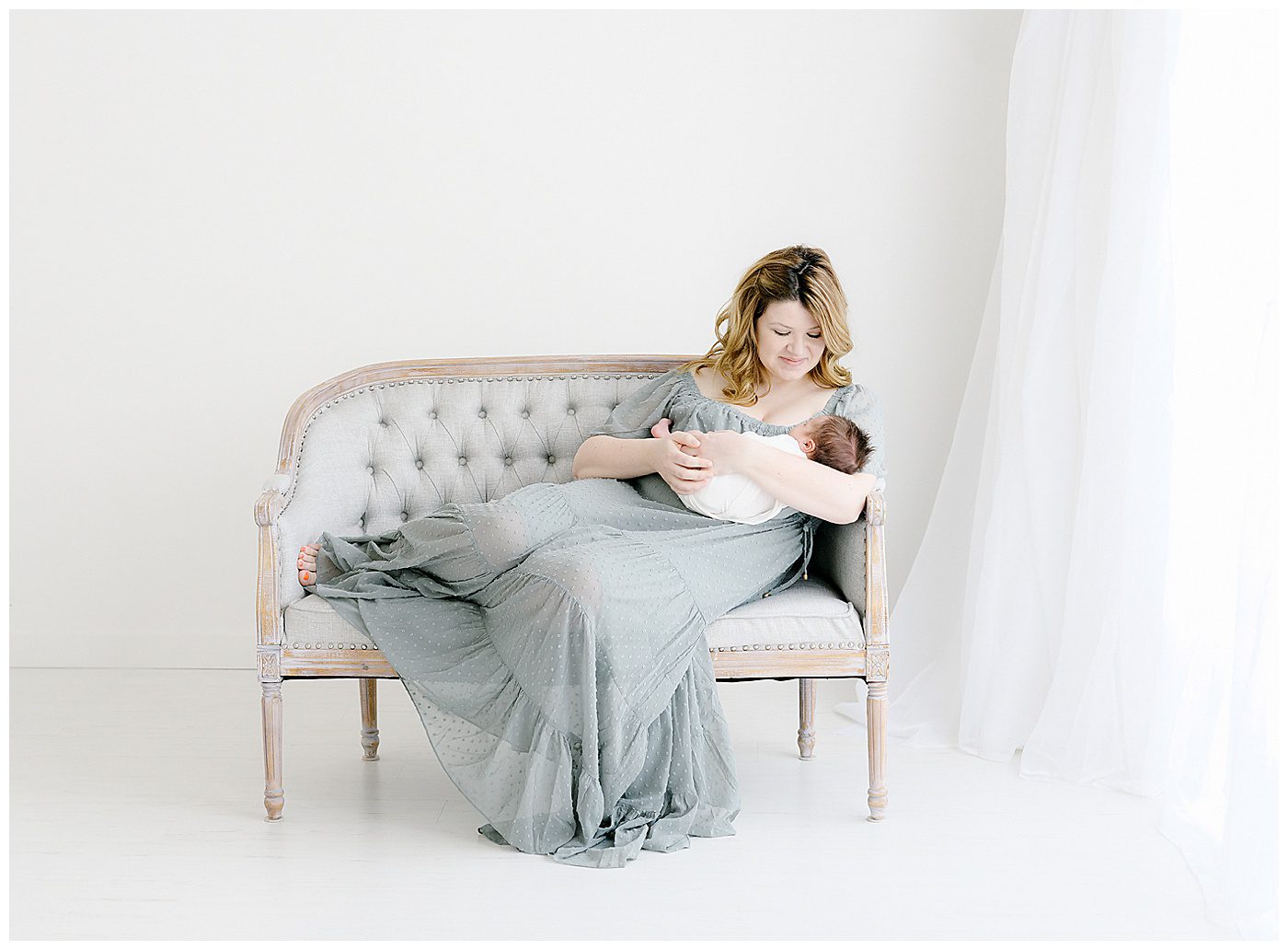 Mom in blue vici dress holding newborn baby boy on settee