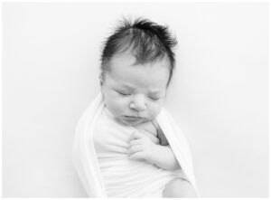 black and white photo of newborn baby boy swaddled in white on a white backdrop