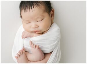 wrapped sleeping newborn on a white blanket with white swaddle