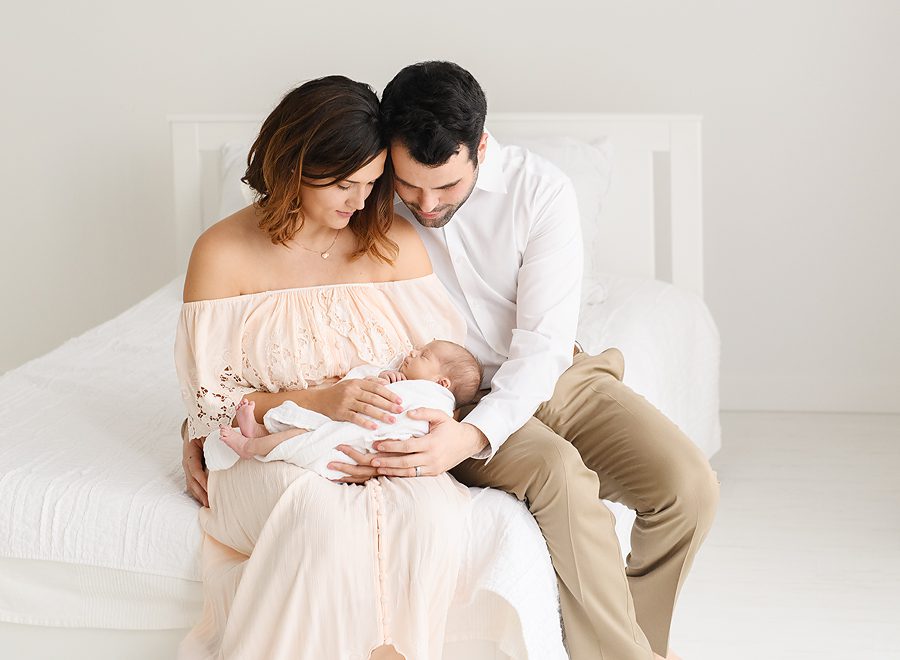 St. Louis Park baby photographer takes photos of mom and dad with newborn baby girl on white bed in studio