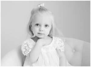 black and white photos of toddler girl in white dress sitting on chair