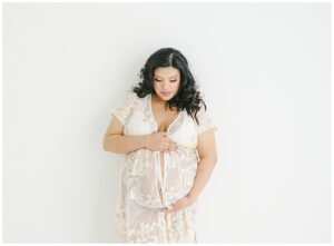 Maternity photo of pregnant mom in floral robe against white wall looking down at her belly by Coon Rapids maternity photographer Melissa Klein