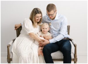Mendota heights newborn photos with mom, dad, and big sister sitting on bench in studio