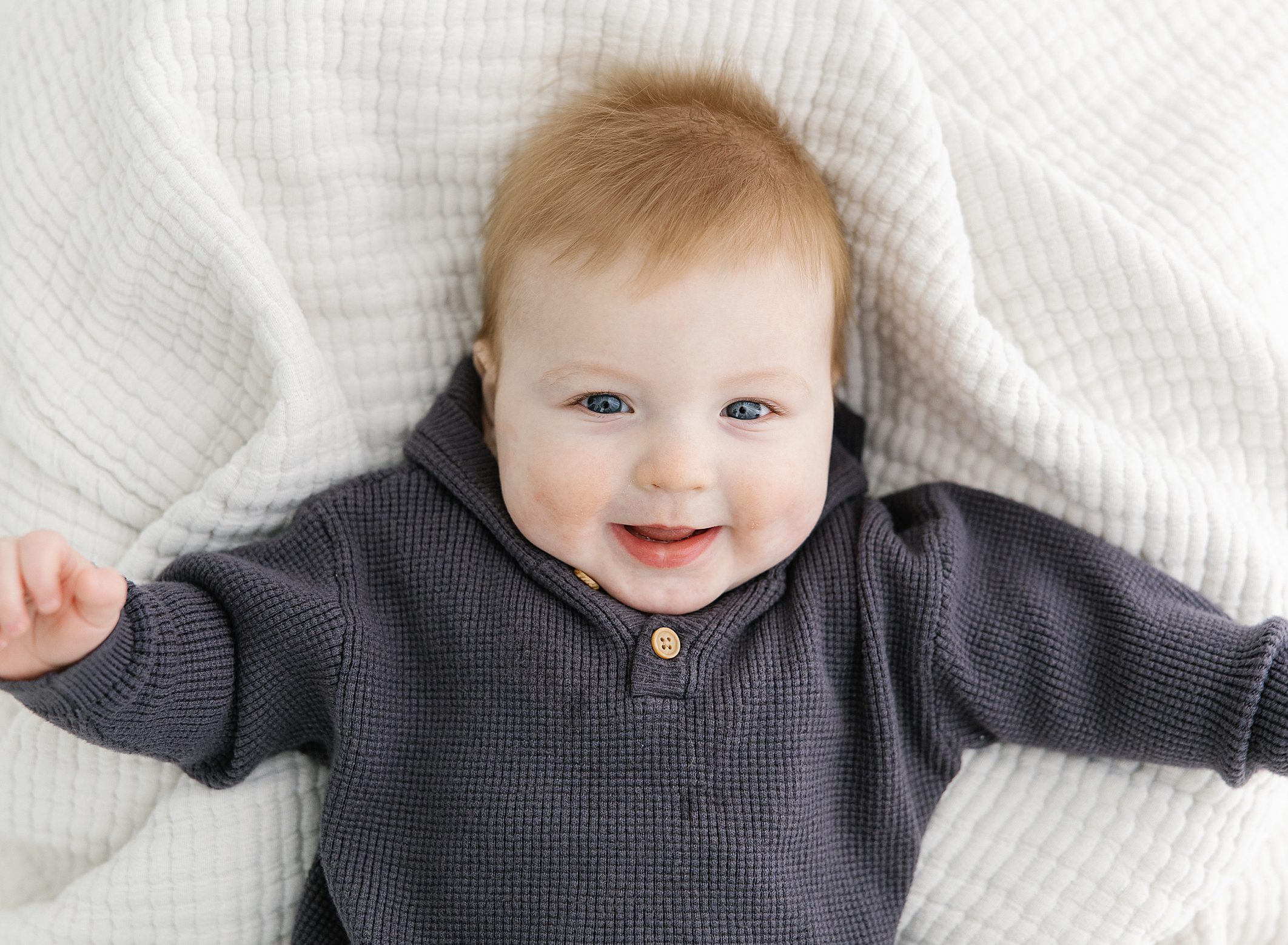 6 month old baby boy with red hair laying on white blank smiling up at the camera